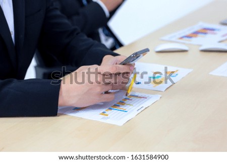 Close up on Businessman hand using mobile phone and working at office with graph data documents on his desk.