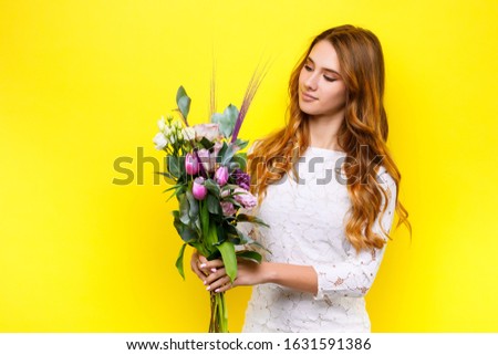 cute girl in white dress looking at bouquet of eustoma flowers on yellow background