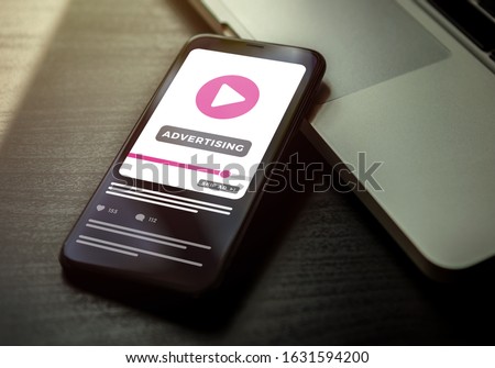 Video Advertising Youtube business concept. Smartphone lying on a dark wooden table with ads media on the screen. Digital marketing with online broadcasting and streaming video advertising content Royalty-Free Stock Photo #1631594200