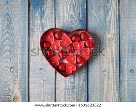 Valentines day background. Red heart shaped box with red candles and candies inside on blue wooden surface. Valentine's day concept. Flat lay, top view, copy space.