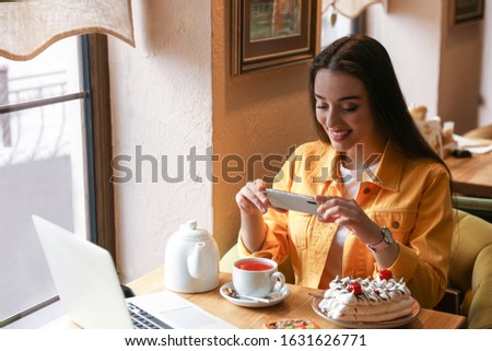 Young blogger taking picture of tea at table in cafe