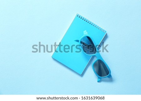 Stylish eyeglasses with notebook on color background