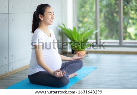 Pregnant women are doing yoga for good health in the living room. Asian pregnant woman practicing yoga on mat. Royalty-Free Stock Photo #1631648299