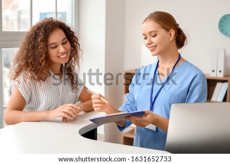 Young female receptionist working with patient in clinic Royalty-Free Stock Photo #1631652733