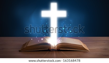 Open holy bible with glowing cross in the middle on wooden deck