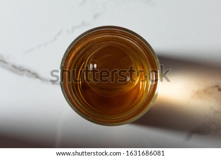 top view of ice cube in glass of whiskey on white marble surface