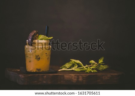 An orange cocktail with a mint leaf on a wooden tray