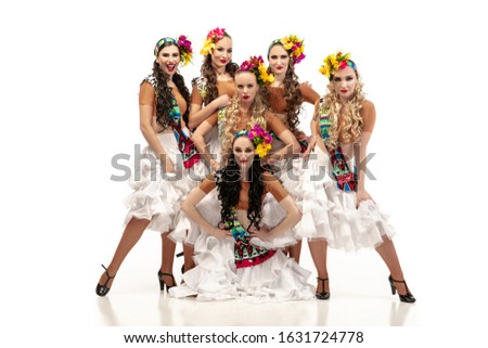 Beautiful young caucasian women in carnival and stylish masquerade costumes with flowers dancing on white studio background. Concept of holidays celebration, festive time, dance, party, having fun.