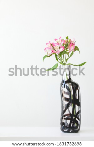 Scene with tall pink alstroemeria in glass vase on table on white wall background. Elegant simple minimal design with copy space.
