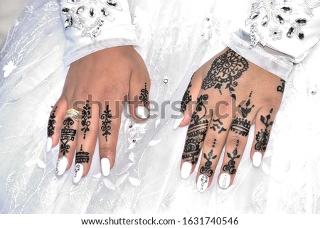 hands of a bride girl on a white dress, white manicure, black henna drawing in oriental style, no tattoo, gold wedding ring on a finger, wedding, salon Royalty-Free Stock Photo #1631740546