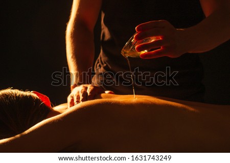 young indian woman lying on the table and getting ayurvedic massage with organic oil or honeyed in dark room.massagist male pouring out client back Royalty-Free Stock Photo #1631743249