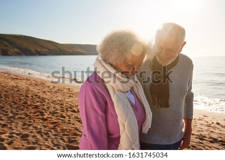 Loving Retired Couple Holding Hands As They Walk Along Shoreline On Winter Beach Vacation Royalty-Free Stock Photo #1631745034