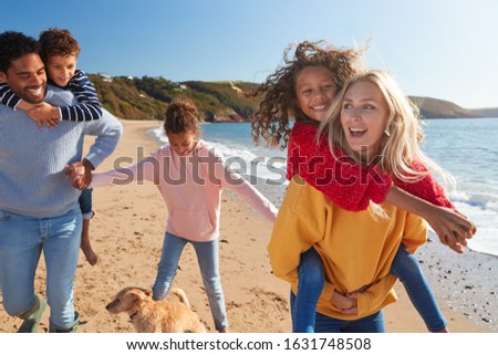Parents Giving Children Piggybacks As They Walk Along Winter Beach Together Royalty-Free Stock Photo #1631748508