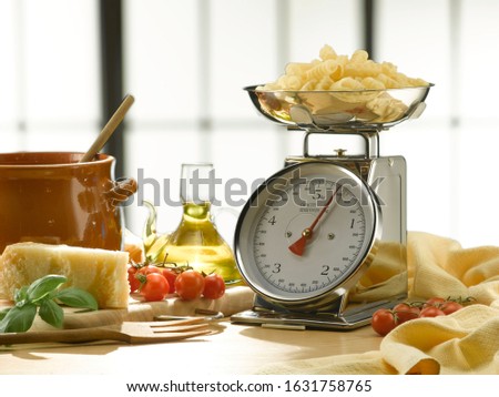 Row pasta on a chromed weighing scale. Close-up on a kitchen table. An industrial-style window is in the background.