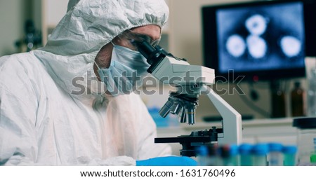 A research scientist working in his laboratory with a sample or specimen and an image of the Wuhan Coronavirus displayed on a computer screen. Royalty-Free Stock Photo #1631760496
