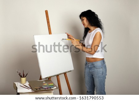 The artist at the easel paints a picture. Attractive girl with a brush paints. A blank canvas for a new painting and an artist with a brush and paints.