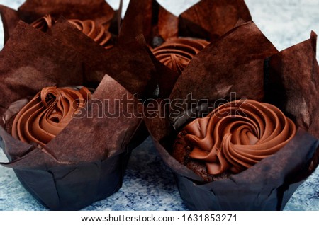 FOUR CHOCOLATE MUFFINS WITH CHOCOLATE CREAM ON PAPER BASKET