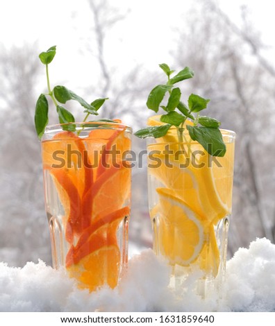glasses with natural lemon and tangerine drink with mint in the snow