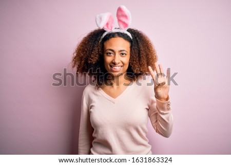 Young african american woman with afro hair wearing bunny ears over pink background showing and pointing up with fingers number four while smiling confident and happy.