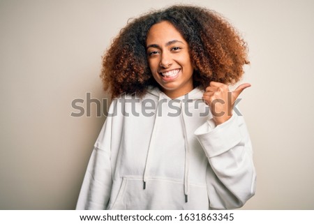 Young african american sportswoman with afro hair wearing sporty sweatshirt smiling with happy face looking and pointing to the side with thumb up.