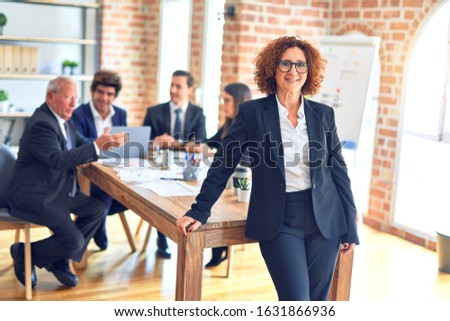 Group of business workers smiling happy and confident working together in a meeting. One of them, standing with smile on face looking at camera at the office.
