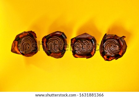 Four muffins with chocolate cream lined up on a yellow background