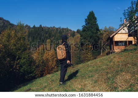 girl photographer with backpack stands on slope and view nature in mountains in fall.