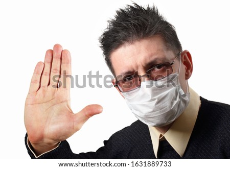 The man in the medical face mask frowns and makes a STOP sign with his hand. His hair stands on end. Isolated on a white background