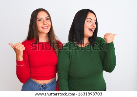 Young beautiful women wearing casual clothes standing over isolated white background smiling with happy face looking and pointing to the side with thumb up.