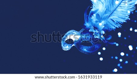 Festive mask with decorative feathers on blue background. Monochrome composition.Mardi Gras concept. Copy space, close-up