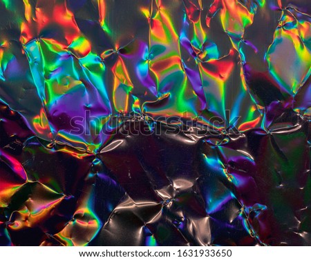 high res full frame macro photo of abstract crumpled iridescent holographic foil background with light leaks. holo color wrinkled material. cool glitter surface with shiny rainbow color blocking feel.