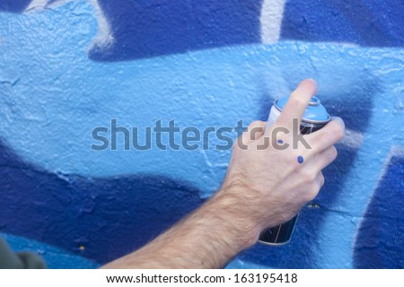 Graffiti artist holding a spray paint can to a wall Royalty-Free Stock Photo #163195418