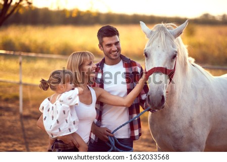 Happy family petting a white horse, enjoying the outdoors.  Fun on countryside, sunset golden hour. Freedom nature concept. 