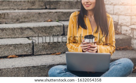 Young pretty woman  with smartphone and cup of coffee sit on city street stairs