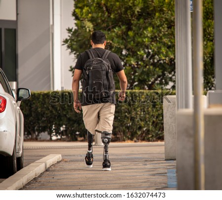 Man with two prosthetic transtibial legs walking in short pants  with backpack away from camera.  Royalty-Free Stock Photo #1632074473