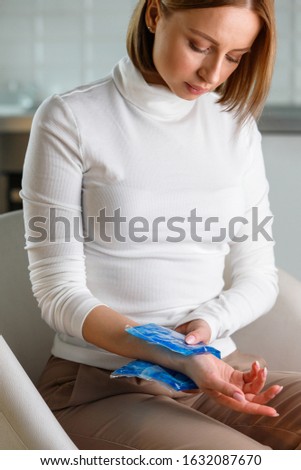 Close up of woman applying cold compress to a her painful wrist caused by prolonged work on the computer, laptop. Carpal tunnel syndrome, arthritis, neurological disease concept. 