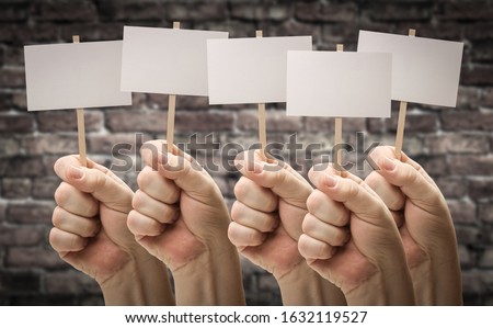Five Male Hands Holding Blank Signs Against Aged Brick Wall.