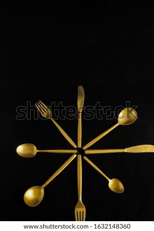 A vertical shot of golden color eating utensils with a pitch-black background