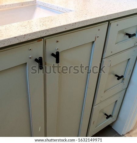 Photo Square frame White countertop with sink and black faucet over cabinets with black handles