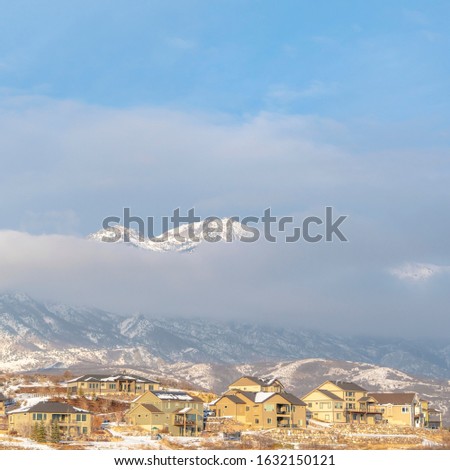 Photo Square Snowy mountain partially covered by thick clouds with houses in the foreground