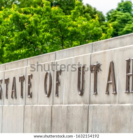 Square frame State Of Utah sign mounted on a wall against vibrant green tree leaves and sky