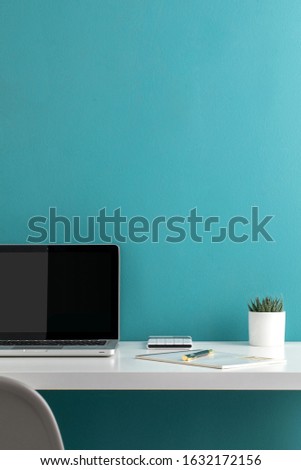 open laptop computer in minimal workspace with office supplies on white table and blue wall background.
