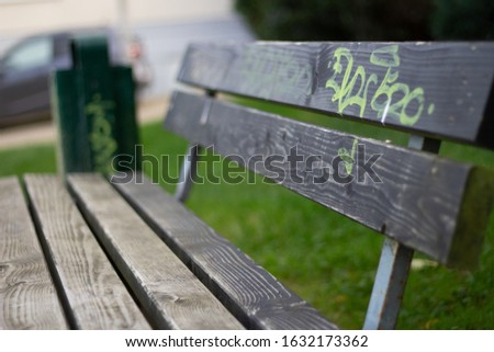 A closeup shot of a wooden bench with a yellow vandalized figure with a blurred background