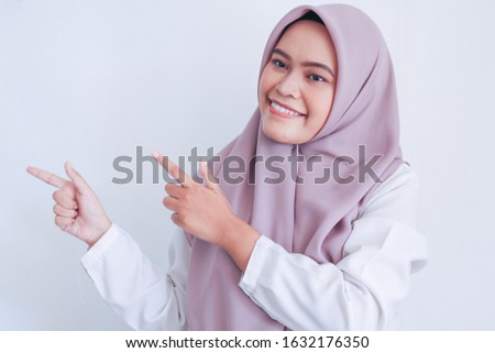 Asian Islam Muslim woman wearing headscarf is pointing finger to blank copy space smile face area. Indonesian woman. Religion concept isolated on gray background.