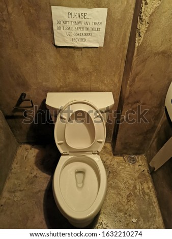 toilet bowl in low light conditions with warning placards. rest room.