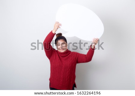 Attractive asian woman in red sweater holding showing blank speech bubble on light gray background, copy space for text