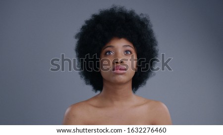 Portrait of beautiful serious african girl interacting with hologram on grey background. Close-up of topless attractive afro-american girl with curly hair using a future touchscreen.