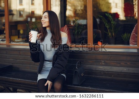 Beautiful girl in a city. Stylish girl drinking a coffee. Lady in a gray dress