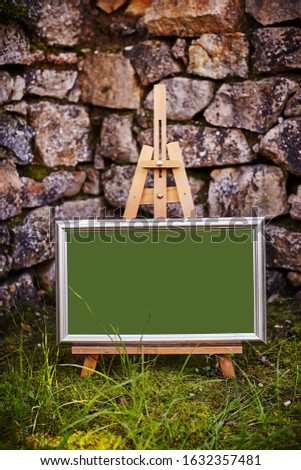 Easel staying om grass and moss near ancient stone walll with copy space Royalty-Free Stock Photo #1632357481