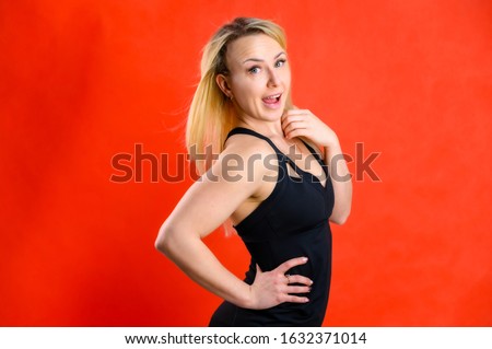 The concept of fashionable fitness. Photo of a beautiful pretty slim woman blonde sportswoman in a tracksuit on a red background. Standing in different poses with emotions and a smile.